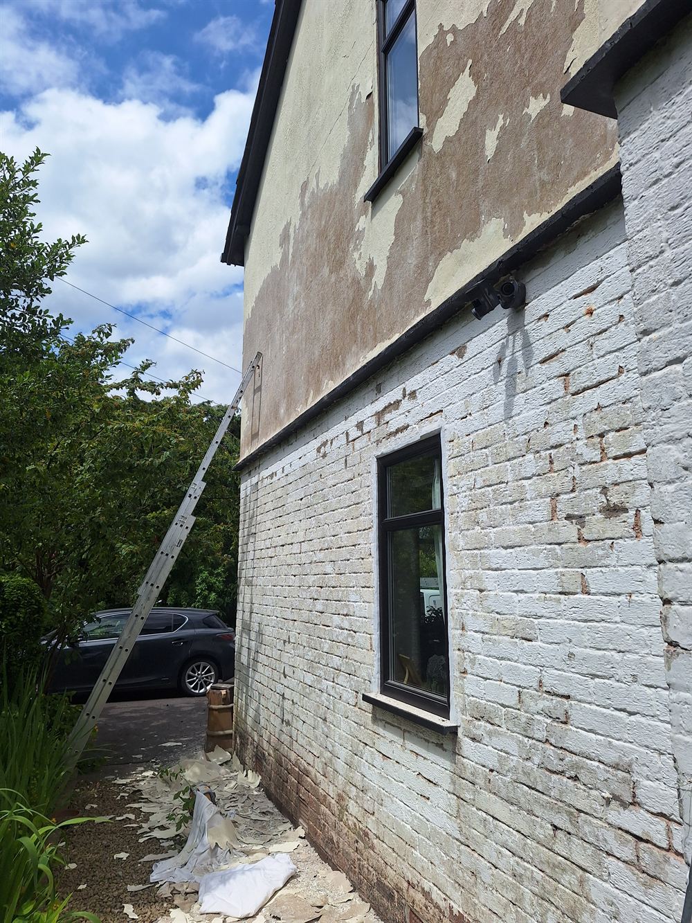 Gable end with render and paint peeling away, part-way through stripping