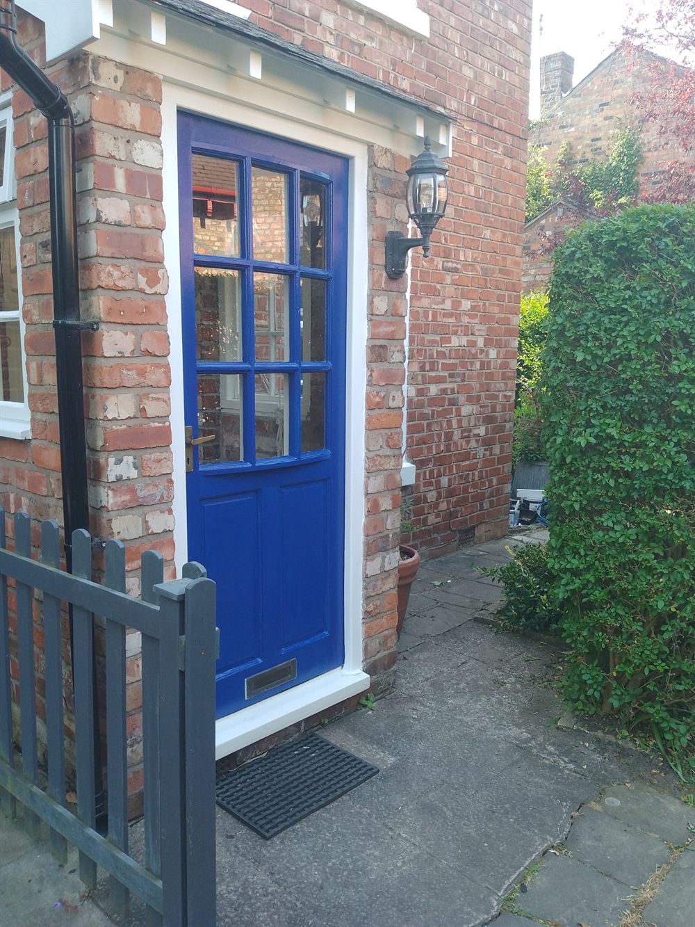 Bright blue painted front door on a brick cottage with a painted gate