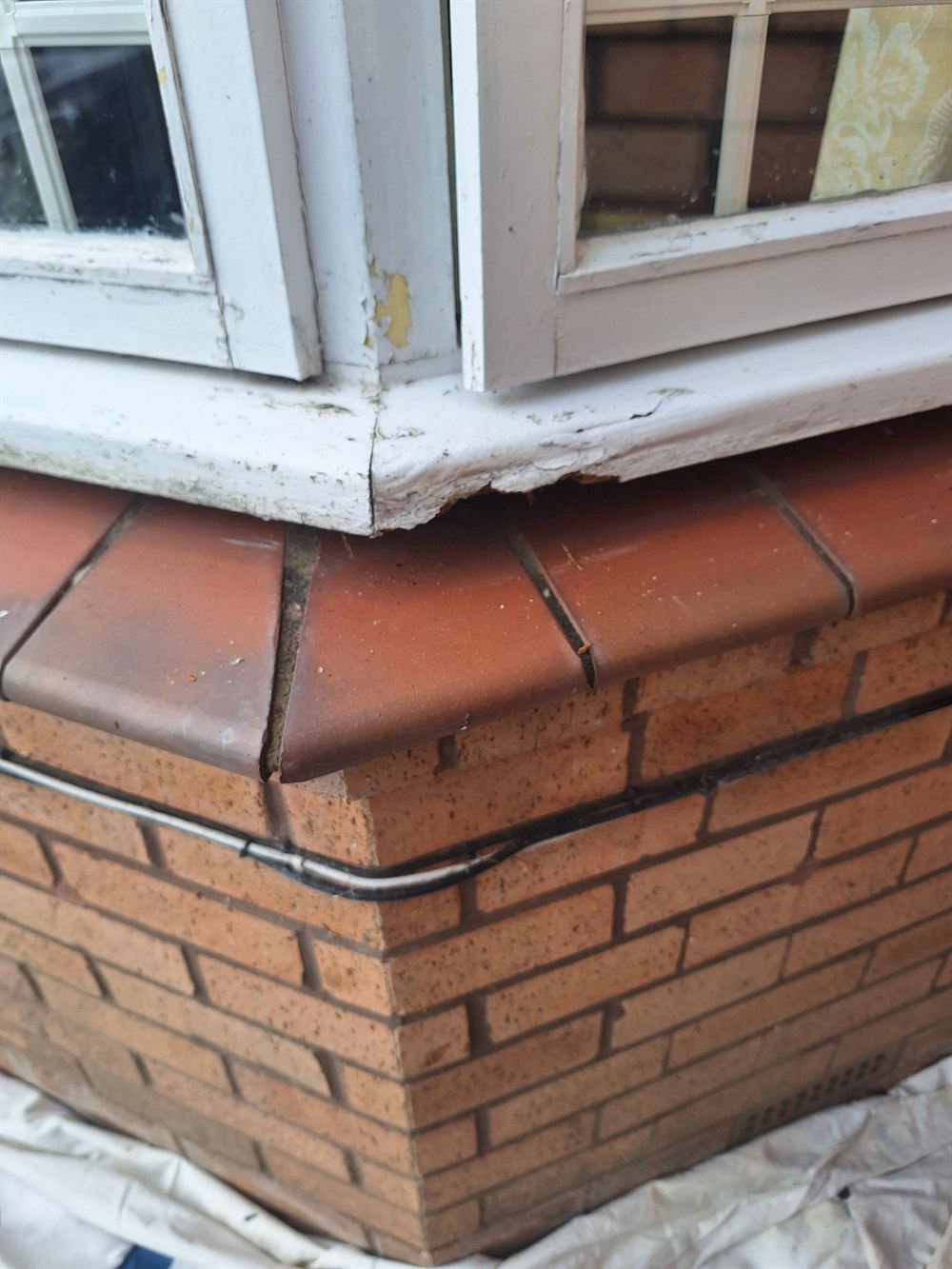 Decayed corner of a painted timber bay window cill, with the paint broken open
