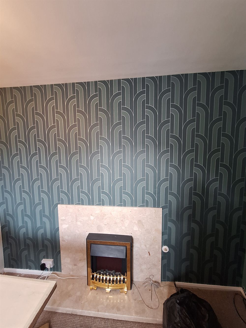 The same chimney breast hung with a teal art deco arch pattern wallpaper